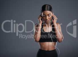 Choose music thatll get you in the right state of mind. Studio shot of a sporty young woman listening to music against a grey background.