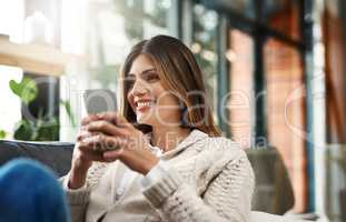 Exciting news to keep you on the edge of your seat. an attractive young woman sending text messages while relaxing on her sofa at home.