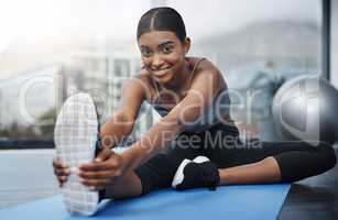 Every good workout starts with a positive attitude. a beautiful young woman smiling while sitting down and doing stretching exercises on her gym mat at home.