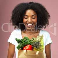 Feed your body well and it will reward you. Studio shot of an attractive young woman holding a bag full of vegetables against a pink background.