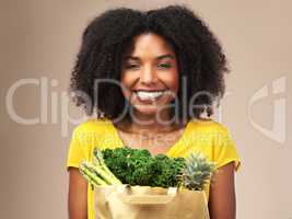 Lots of greeny goodness. Studio shot of an attractive young woman holding a bag full of vegetables against a brown background.