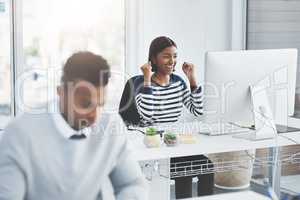 Even the smallest victories deserve to be celebrated. a young businesswoman celebrating at her office desk with a colleague working in the foreground.