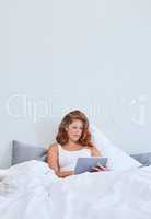 Catching up on some leisurely time. a young woman using a digital tablet while relaxing in bed at home.