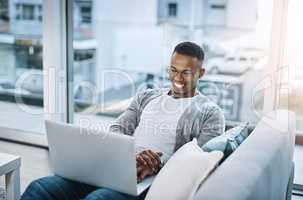 Things are getting really interesting now. a handsome young man using his laptop while sitting on a sofa at home.