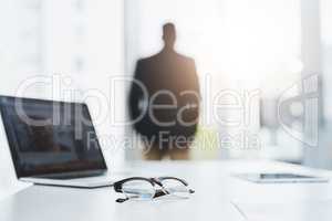 In search of greater opportunities for business. Closeup shot of a pair of spectacles and a laptop on a table in an office with a businessman in the background.