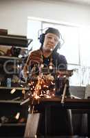 Taking the edge off. an attractive young female artisan using an angle grinder in her workshop.