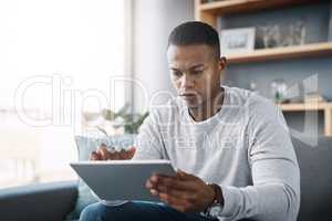 Quickly arranging my schedule for the upcoming week. a handsome young man using his digital tablet while sitting on a sofa at home.