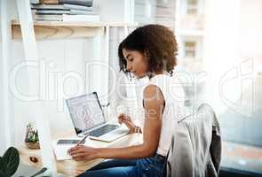 Making sure she doesnt forget. an attractive young businesswoman writing in her notebook while working in her home office.
