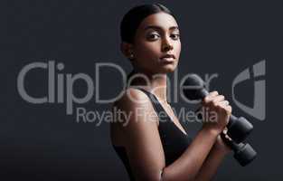 Focus and discipline are the greatest strengths you can possess. Studio portrait of a young sportswoman doing dumbbell exercises against a gray background.