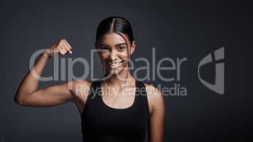 Going from strength to strength everyday. Studio portrait of a young sportswoman flexing her bicep against a gray background.