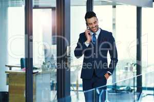 He takes the time to talk to his clients. a young businessman talking on a cellphone in an office.