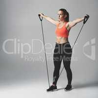 Resistance training is good for the whole body. Studio shot of an athletic young woman working out with a resistance band against a grey background.