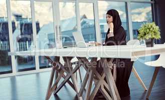She always gets the job done. Full length shot of an attractive young arabic businesswoman working on her laptop in the office.