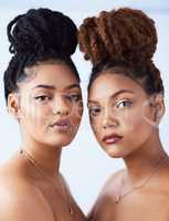 Hair back and looking gorgeous. Studio shot of two beautiful young women posing against a grey background.