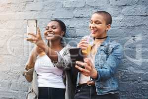 Cuteness overload. two young women standing beside a building smiling and taking selfies while holding their cool drinks.