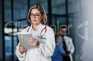 Connected and on call. a young doctor using a digital tablet in a hospital with her colleagues in the background.