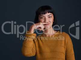 Whats life without a bit of silliness. Studio shot of an attractive young woman making a mustache with her finger against a dark background.