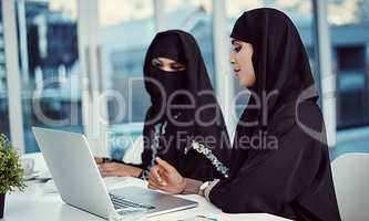 Communication and teamwork go hand in hand. two young arabic businesswomen working on a laptop in their office.