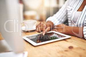 Female african hand using a tablet at a desk doing office work. Closeup of a professional woman browsing on social media while having a cup of tea or coffee. Businesswoman doing research online.