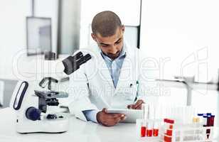 Scientist writing DNA results from microscope test on a tablet.Professional male doctor in a lab working with research tubes.Man in a modern laboratory doing medical science data analysis.