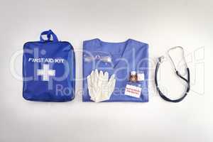 Medical kit, doctor scrubs and hospital equipment on a table for safety and healthcare in a clinic from above. Flat and top view of a bag, uniform and stethoscope on a desk before a procedure