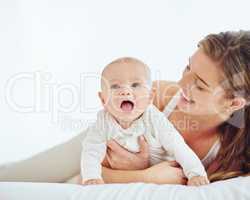 Loving mother and baby bonding at home, playing while relaxing on a bed together. Happy parent being affectionate with her newborn son, embracing him and sharing precious moments of parenthood