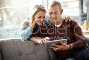 Bit of browsing, lots of bonding. a mature couple using a digital tablet while relaxing together on the sofa at home.