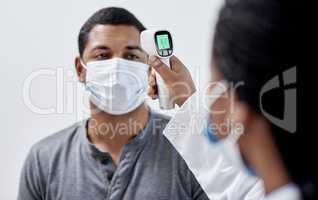 Male covid patient getting his temperature taken with medical equipment by a doctor in hospital consultation room. Man wearing mask and health care professional pointing digital infrared thermometer.