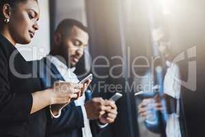 Making connections that will carry them further to the top. two businesspeople using their cellphones in an office.