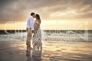 Kisses at sunset. Full length shot of an affectionate young couple kissing while standing on the beach.