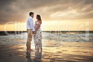 You are all I want to look at. Full length shot of an affectionate young couple holding hands while standing face to face on the beach.