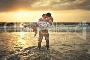 Kiss me like you mean it. Full length shot of a handsome young man kissing his girlfriend while carrying her on the beach.