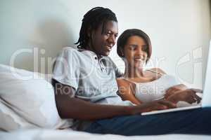 Now that looks pretty interesting. an expecting young couple using a laptop together while relaxing in bed at home.