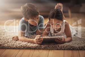 Digitizing playtime. an adorable brother and sister using a digital tablet together on the floor at home.