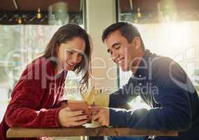 If it makes you happy, share it. a young man and woman using a mobile phone together on a date at a coffee shop.