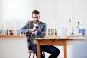 Communication is key when working remotely. a handsome young businessman sending a text message while sitting in the home office.