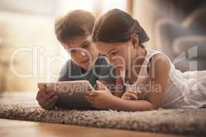 No chance of boredom with touchscreen technology. an adorable brother and sister using a digital tablet together on the floor at home.