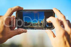 Landscapes are my favorite to capture. an unrecognizable man taking a photo of the city with his cellphone outside.