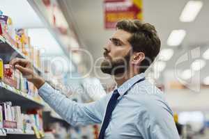Looking at the top shelf. a handsome young man looking for medication in a pharmacy.