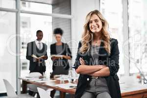 Success continues to follow her. Portrait of a young businesswoman standing in an office with her colleagues in the background.