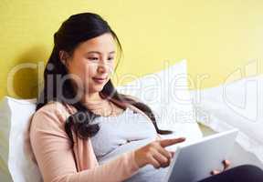 Browsing for all her baby essentials. a pregnant woman using a digital tablet at home.