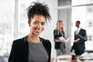 Taking big steps in the right direction. Portrait of a young businesswoman standing in an office with her colleagues in the background.