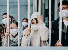 Foreign people in isolation wearing covid face mask at the border or in quarantine or airport looking unhappy, upset and angry. Poor refugees, immigrants and tourists stuck behind a gate in lockdown