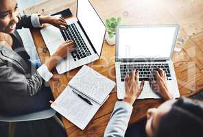 Keeping notes in ink and on screen. High angle shot of two businesswomen working on laptops in an office.