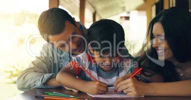 Kids have a way of reminding you of childhood. a young family colouring in together by the table outside.