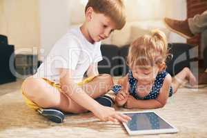 Playtime in the age of the app. an adorable brother and sister using a digital tablet together on the floor at home.