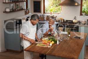 Cooking should be a leisurely experience. a happy mature couple drinking wine while cooking a meal together at home.