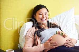 Motherhood is such a beautiful blessing. Portrait of a pregnant woman lying down with wooden baby blocks on her belly at home.