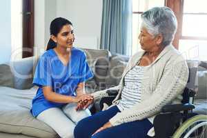 Just keep being optimistic and everything will be alright. a worried looking elderly woman seated in a wheelchair while a female nurse holds her hand for support inside at home during the day.