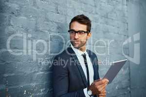 Connectivity unlocks doors. a handsome young businessman using his tablet while standing against a grey facebrick wall.